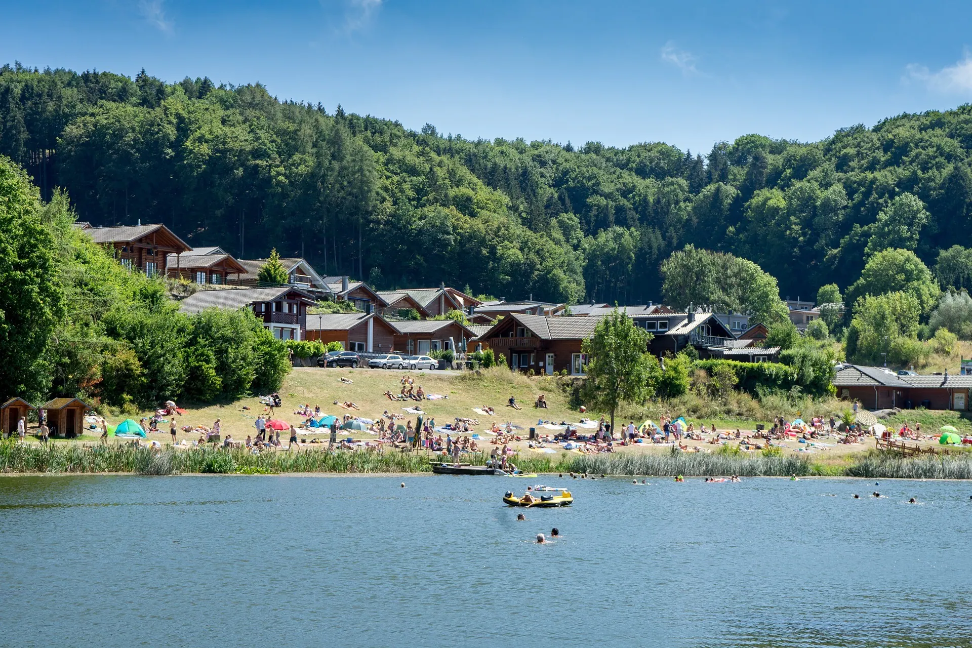 Der Riedener Waldsee mit Liegewiese, Badestrand und den Ferienhäusern am Ufer